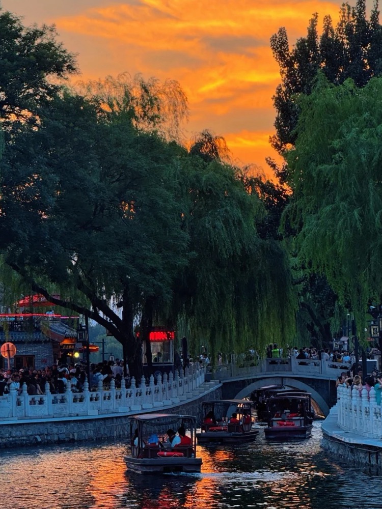 Boats crossing Shichahai beneath an orange Beijing sunset
