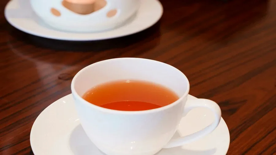 A cup of amber Chinese tea beside a white teapot and warming stand on a wooden table