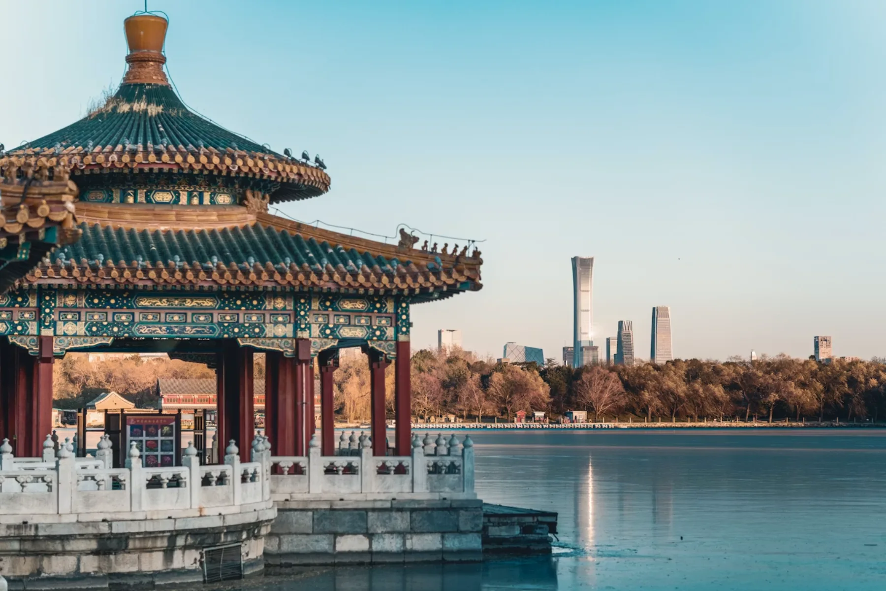 A traditional Beijing pavilion faces the modern China Zun skyline across the lake.