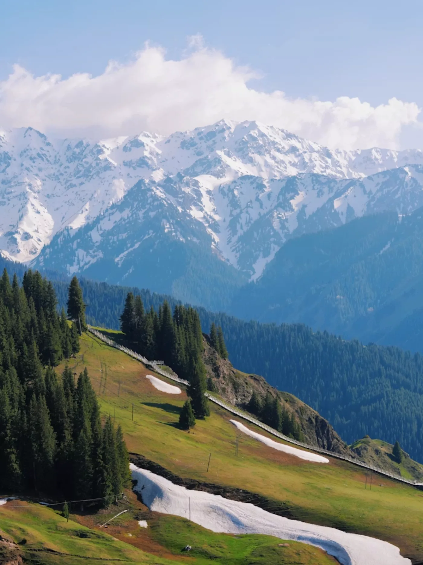 Snow-covered mountains and alpine forest frame a highland route in western China.