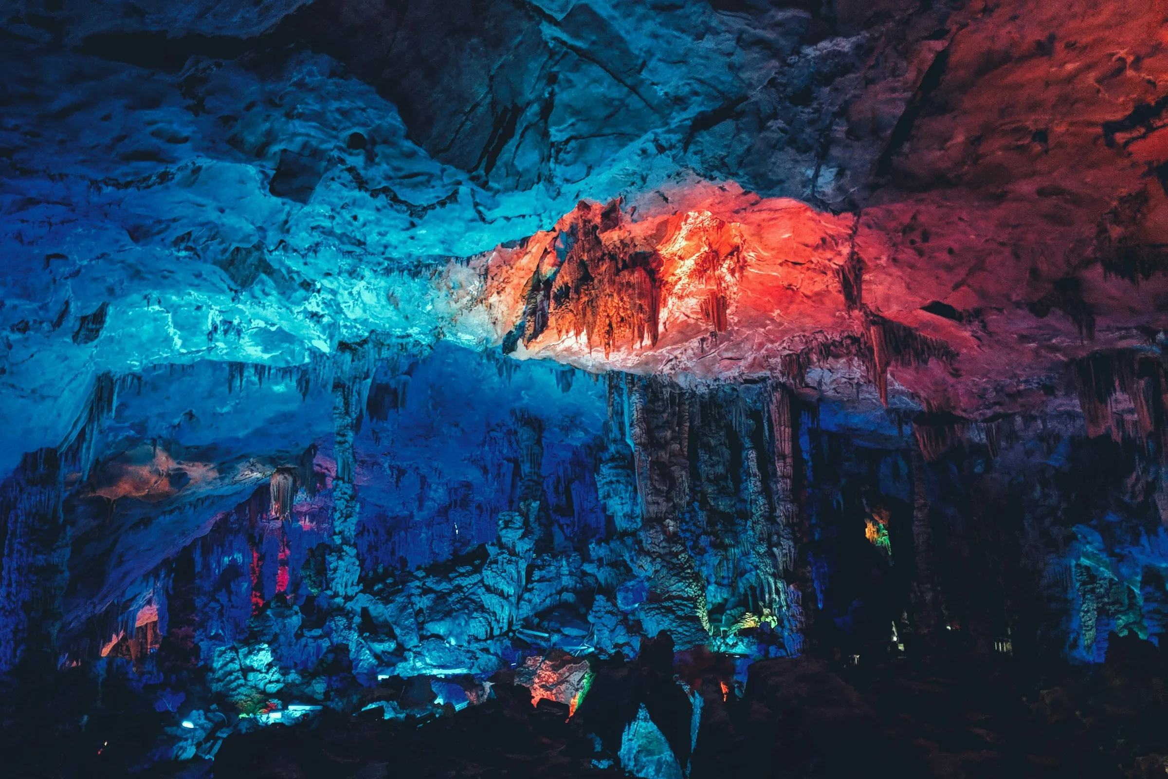 Limestone formations under blue and red lighting inside Reed Flute Cave
