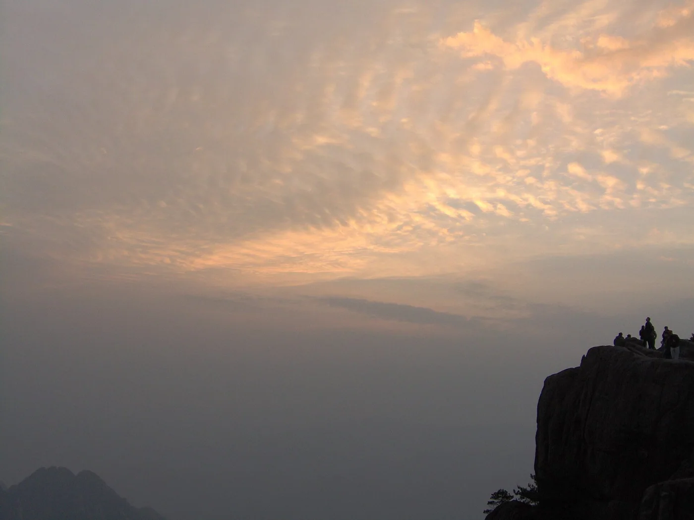 Visitors watching a warm sunrise from a rocky Huangshan viewpoint