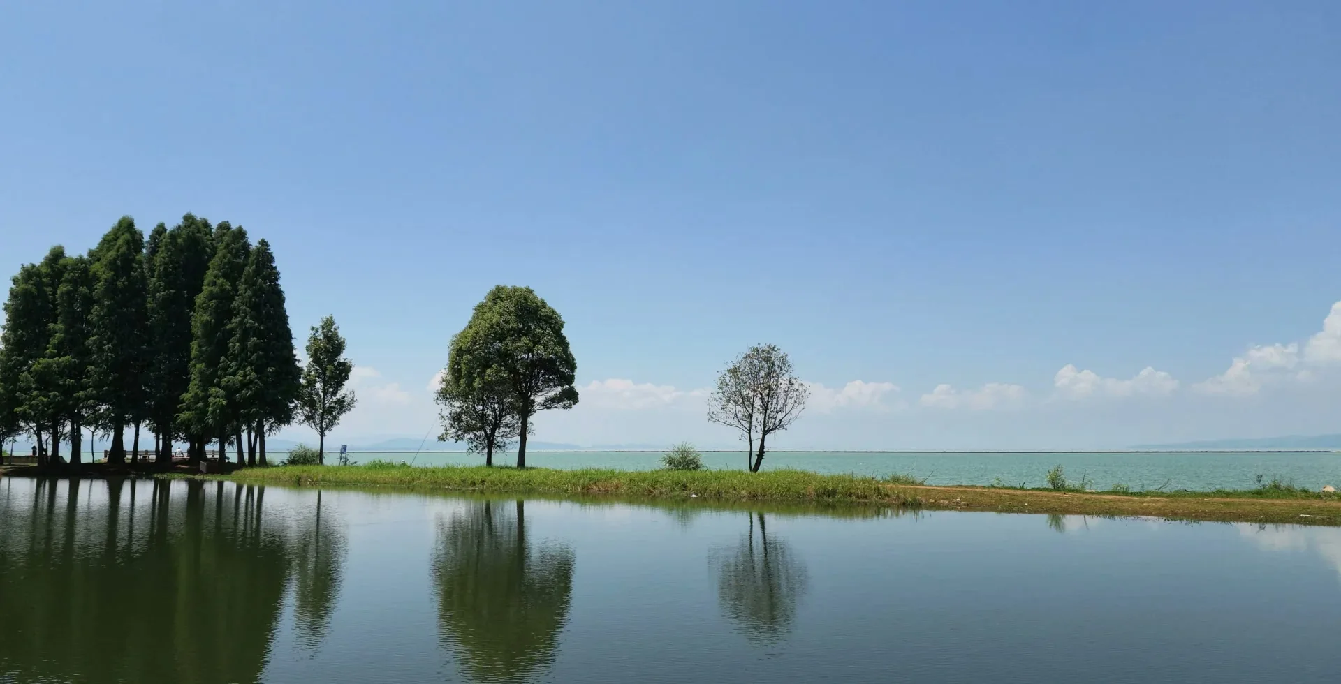 Trees and distant hills reflected along the shore of Dianchi Lake in Kunming