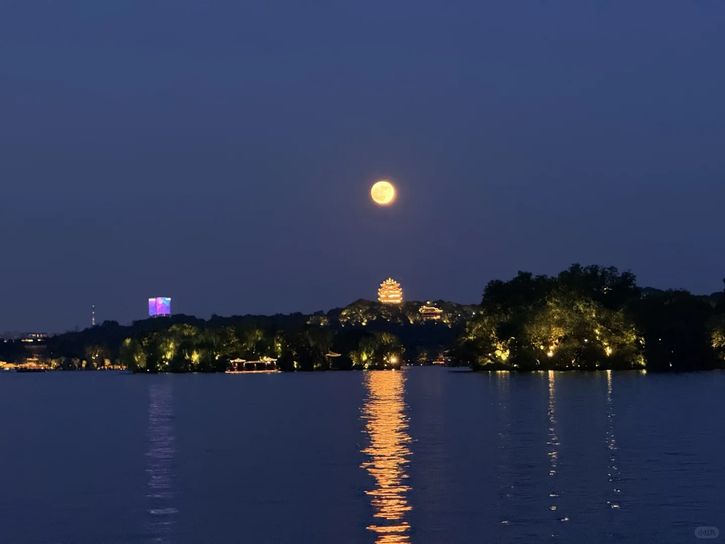 Full moon above the illuminated West Lake shoreline in Hangzhou