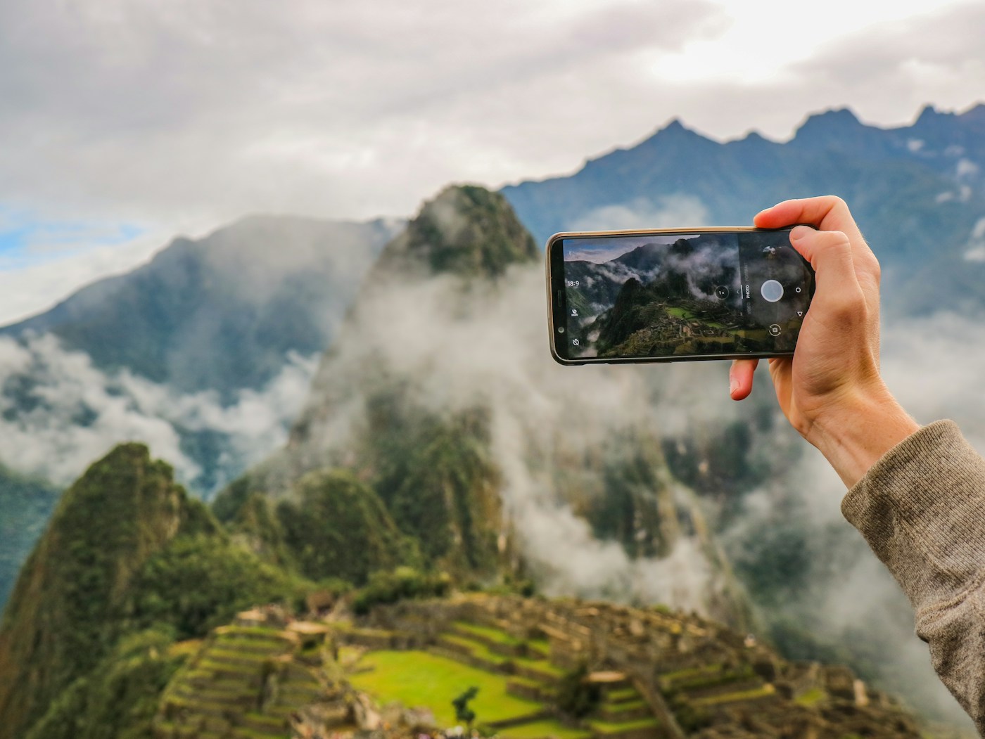 A hand holding a smartphone, photographing misty mountains