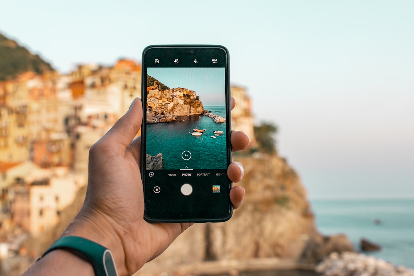 A traveler holding a smartphone while photographing a coastal town