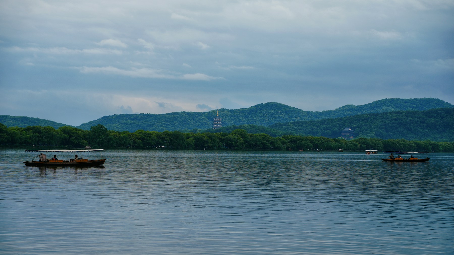 Wooden boats crossing West Lake with green hills behind Hangzhou