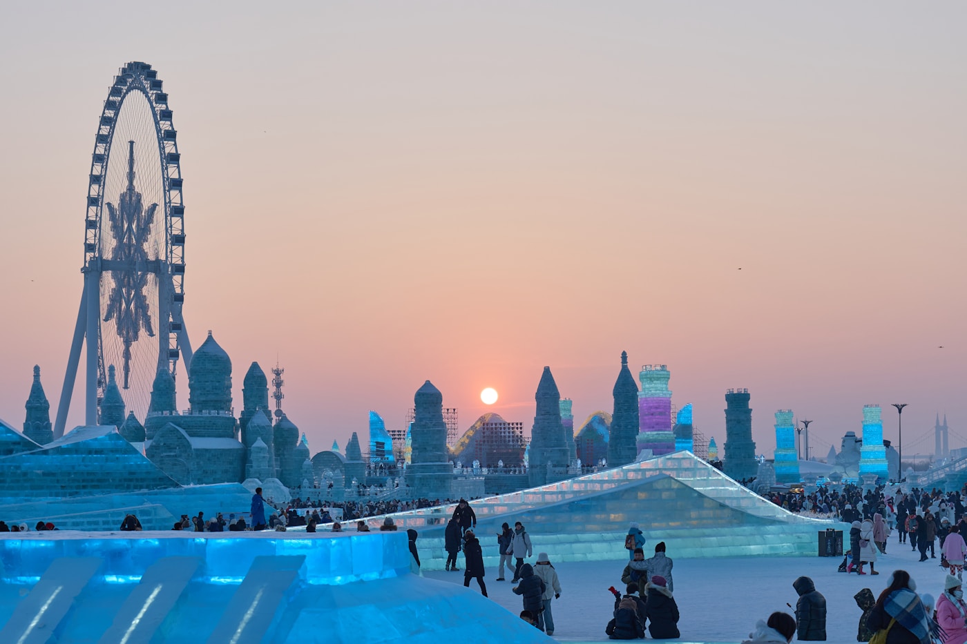 Die Ice and Snow World in der Abenddämmerung – ein Riesenrad und eine Gruppe bunt illuminierter Eistürme